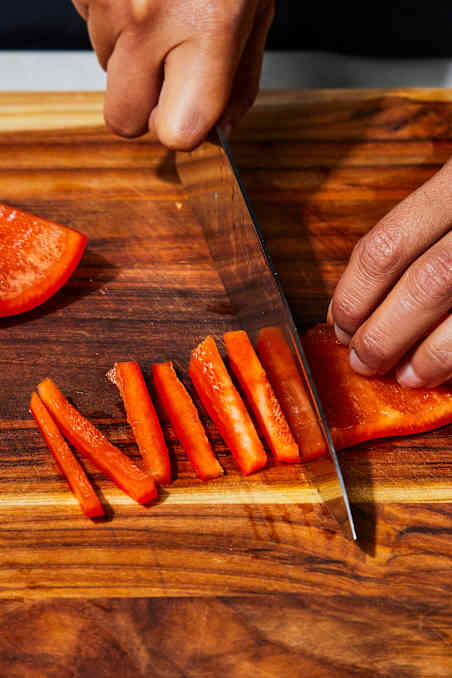 a knife cuts red bell pepper into strips